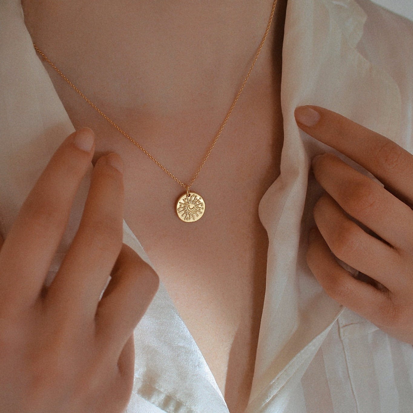 Zarte goldene Halskette mit rundem Anhänger und Sonnen-Mond-Motiv auf der Haut getragen