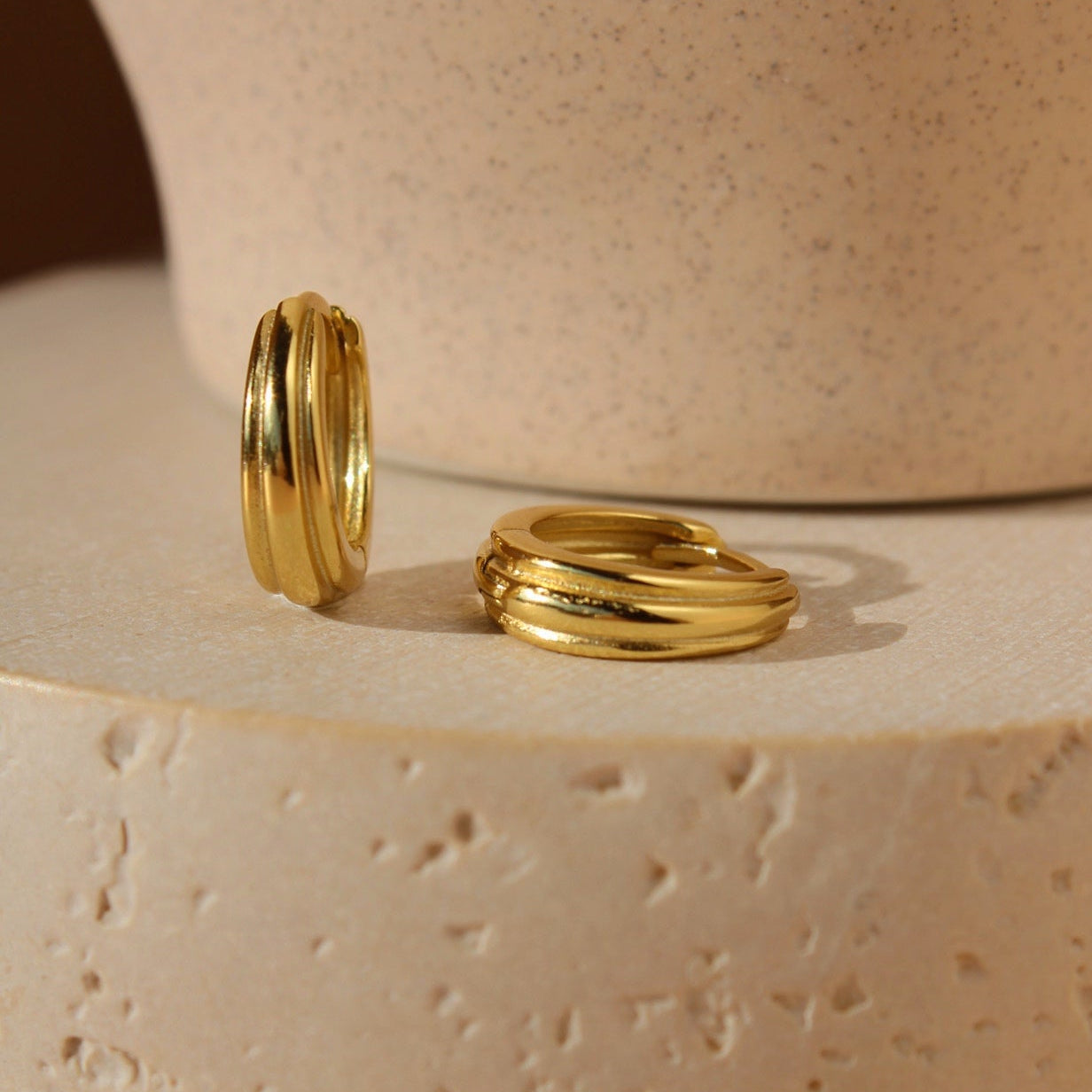 Goldene Creolen mit organischer, mehrlagiger Form auf hellem Steinpodest